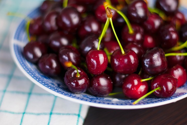 A bowl of cherries on a table with a napkin partially underneath. 