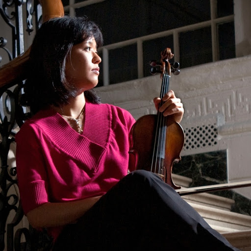 the musician sits with her violin on a spiral staircase