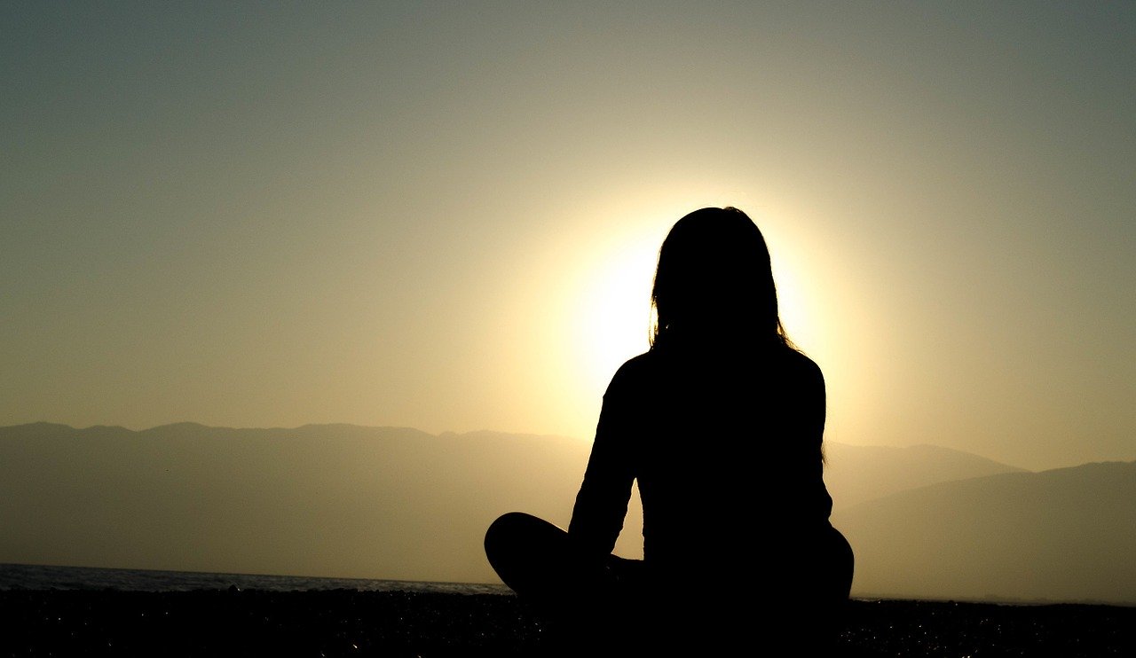 A woman in shadow meditating while the sun rises 