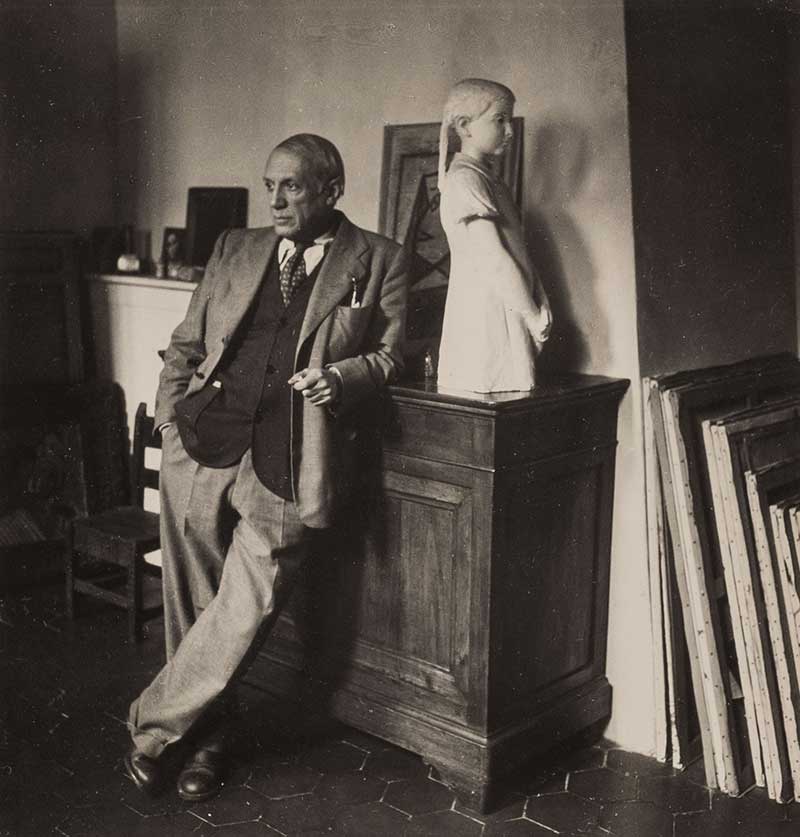 Picasso leaning against a statue and several canvases