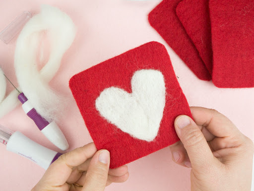 hands holding a red and white felted coaster with a heart shape