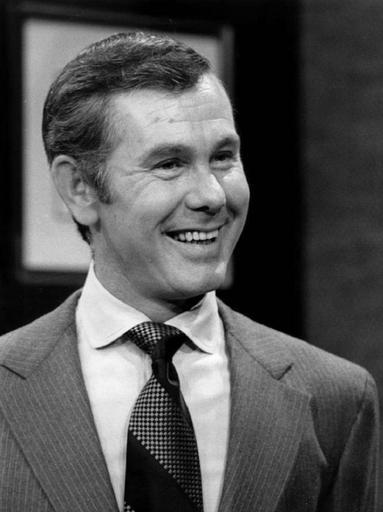 black and white photo of Johnny Carson smiling, in a suit and tie. 