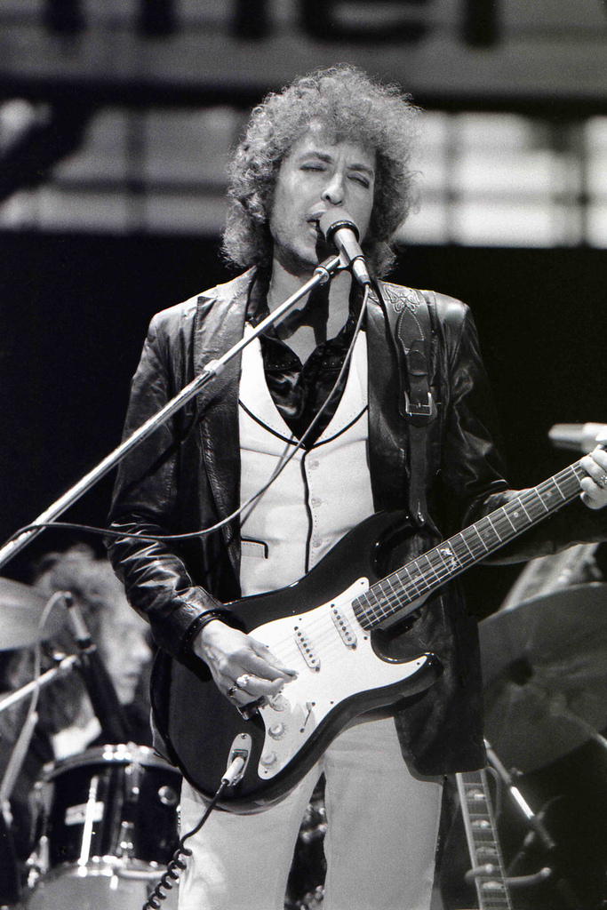 black and white photo of Bob Dylan in 1978 singing into a microphone and holding an electric guitar