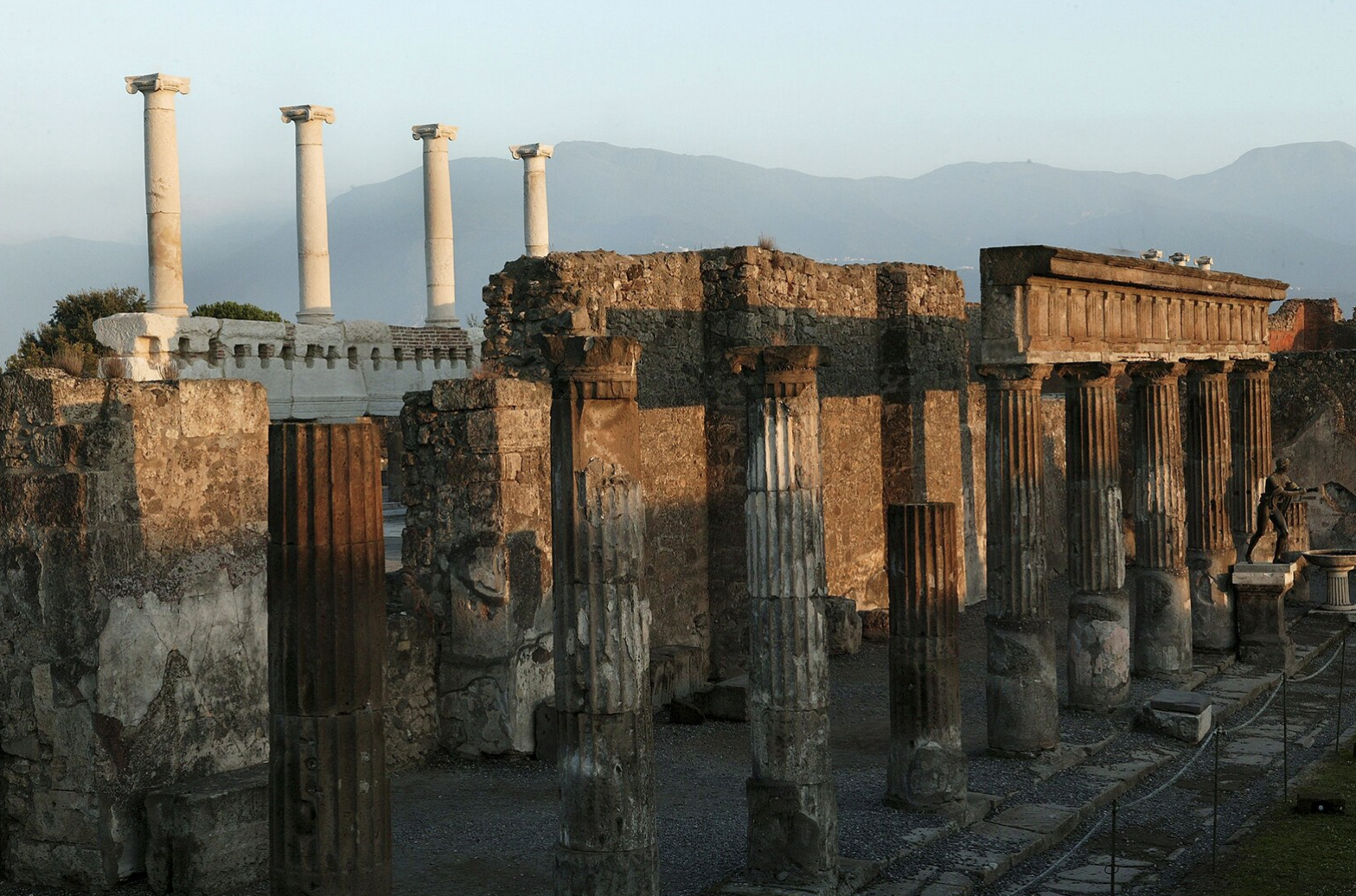 The ruins of a building with many pillars set against the backdrop of foggy mountains. 