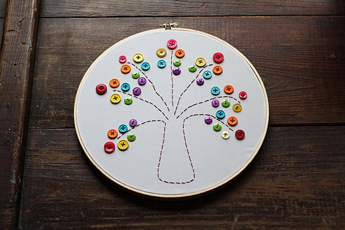 An embroidery hoop with a simple outline of a tree stitched into it and decorated with buttons for the leaves. 
