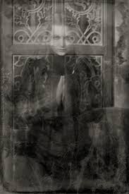 the ghostly figure of a woman looks transparent against an ornate background. Black and white photograph. 