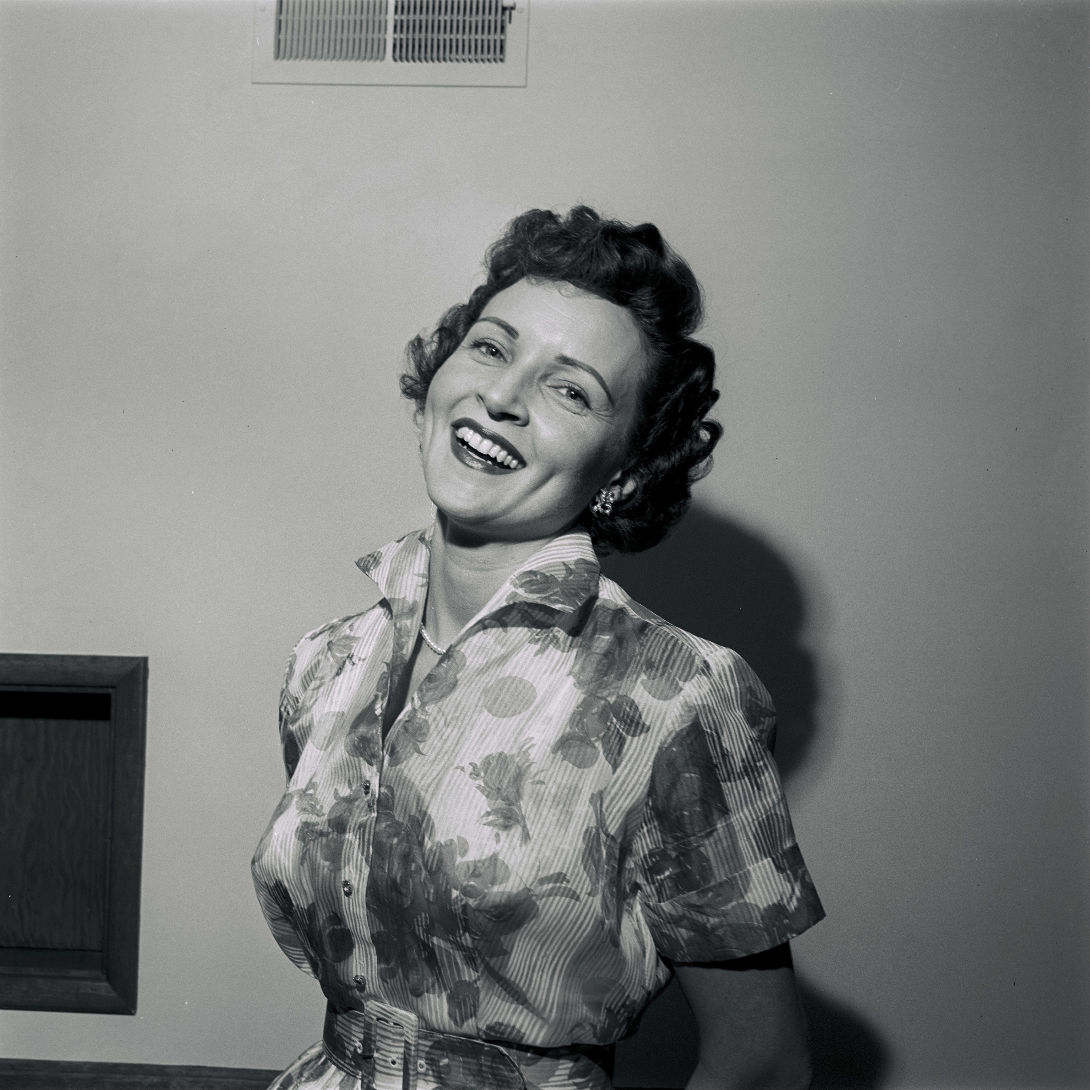 Black and white photo portrait of a young Betty White in a floral dress, smiling