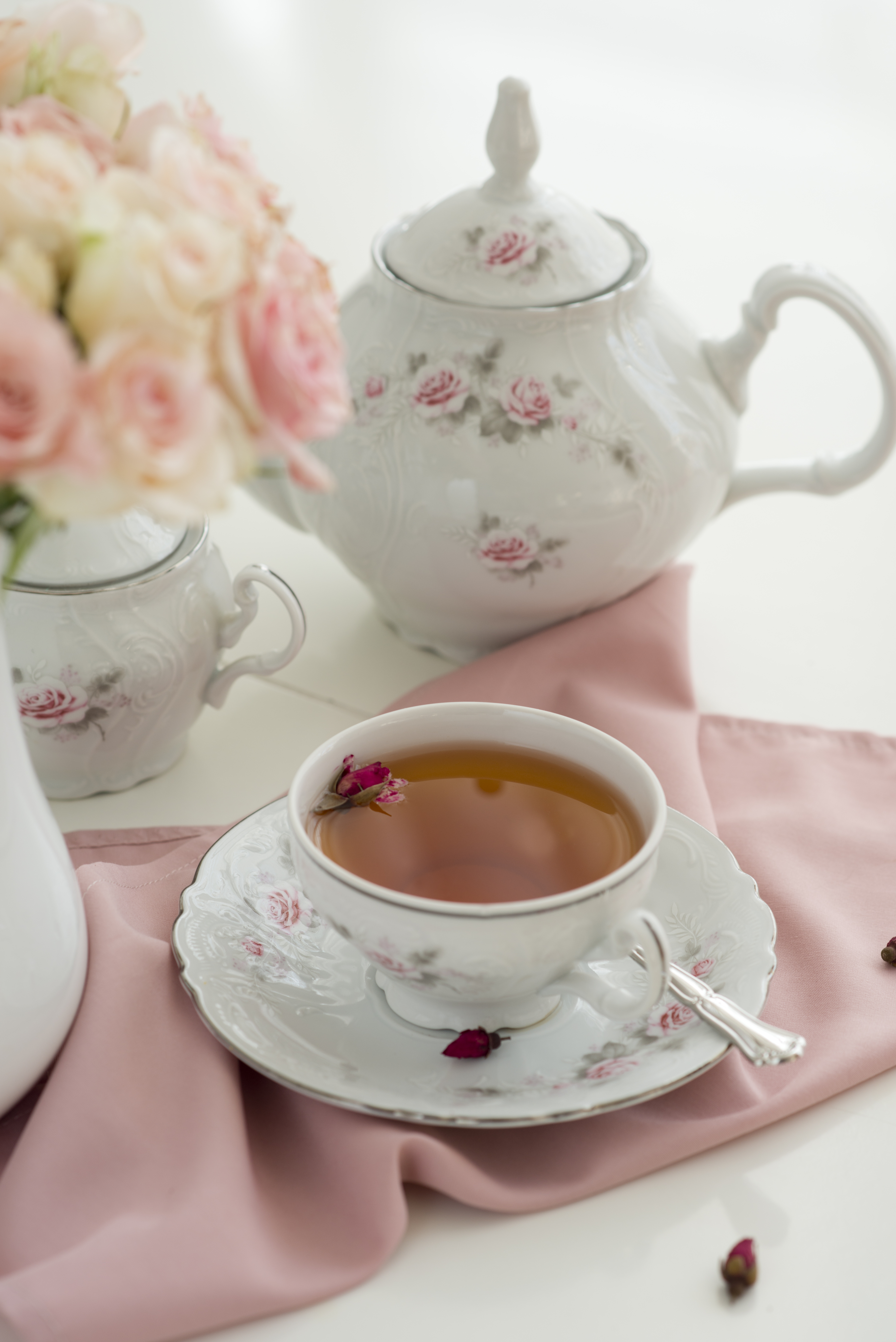 color photo of a pink and white tea set with a full cup of tea and a vase of roses