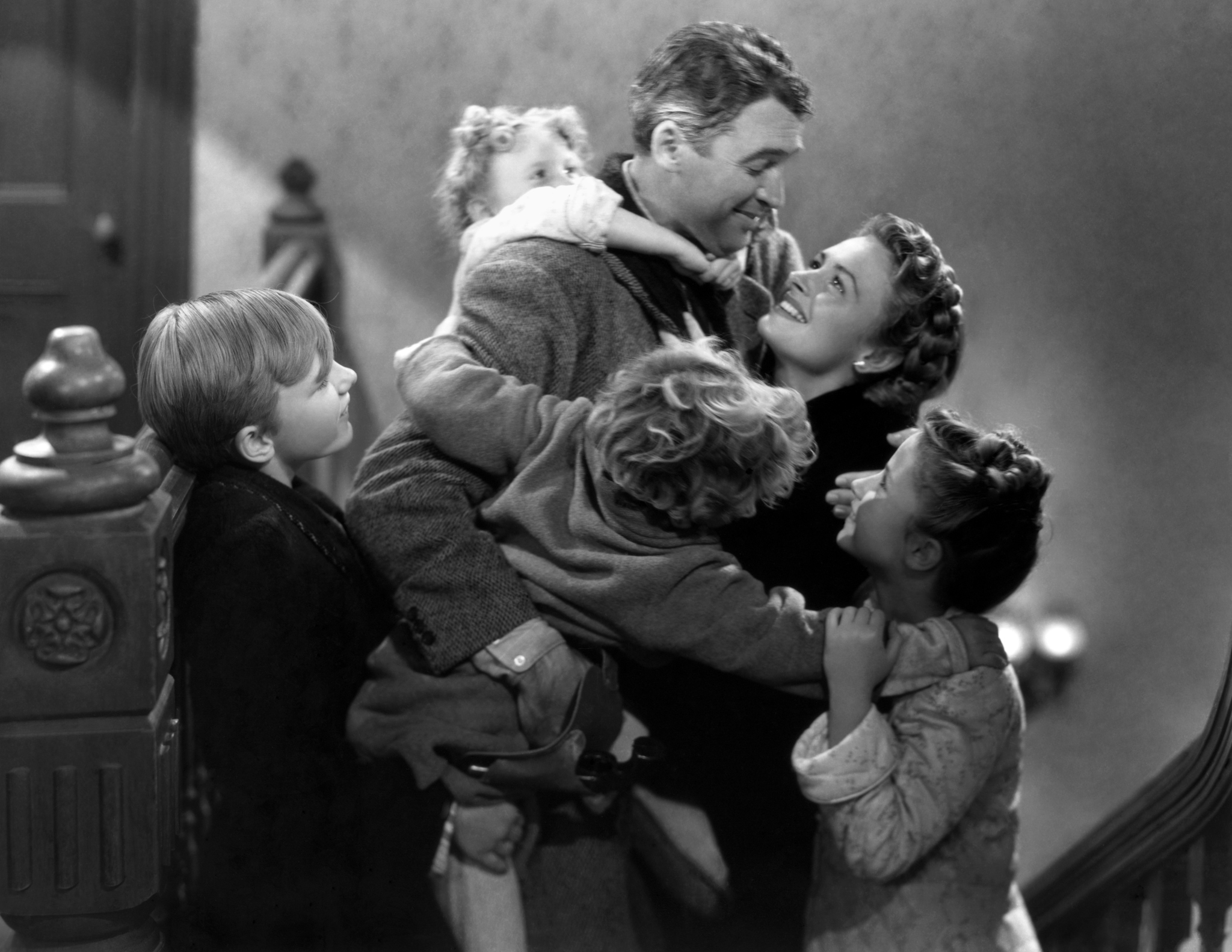 black and white still from It's a wonderful life showing a husband and wife hugging with their children hugging them 