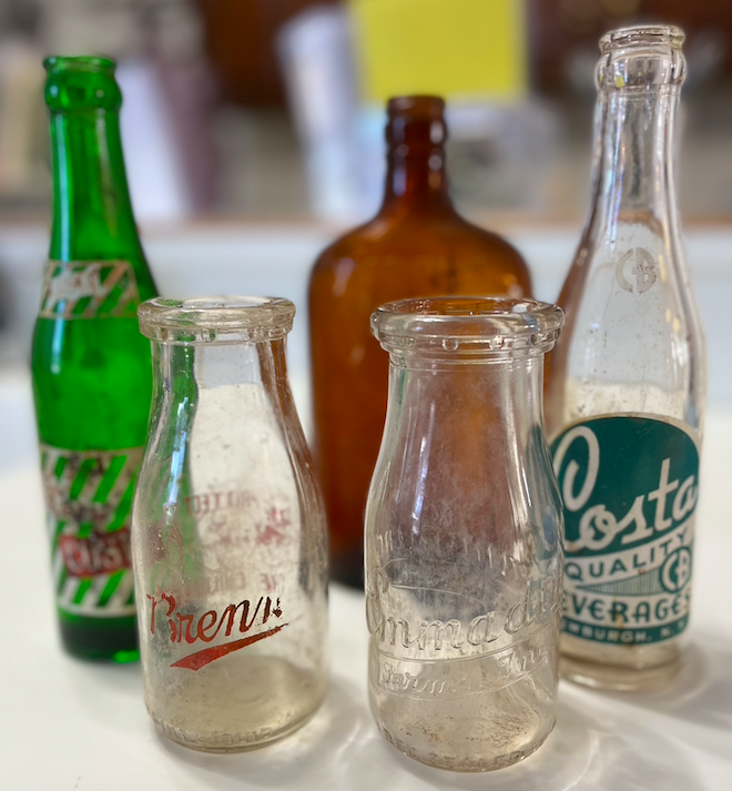 four glass bottles, three clear, on green and one brown sit on a white table. 