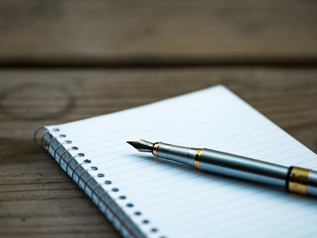 color photo of a fountain pen resting on a notebook which sits on a wood table 