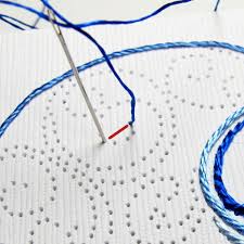 White cardstock with holes pierced in a swirly abstract pattern. A need is stuck through starting to embroider blue thread. 