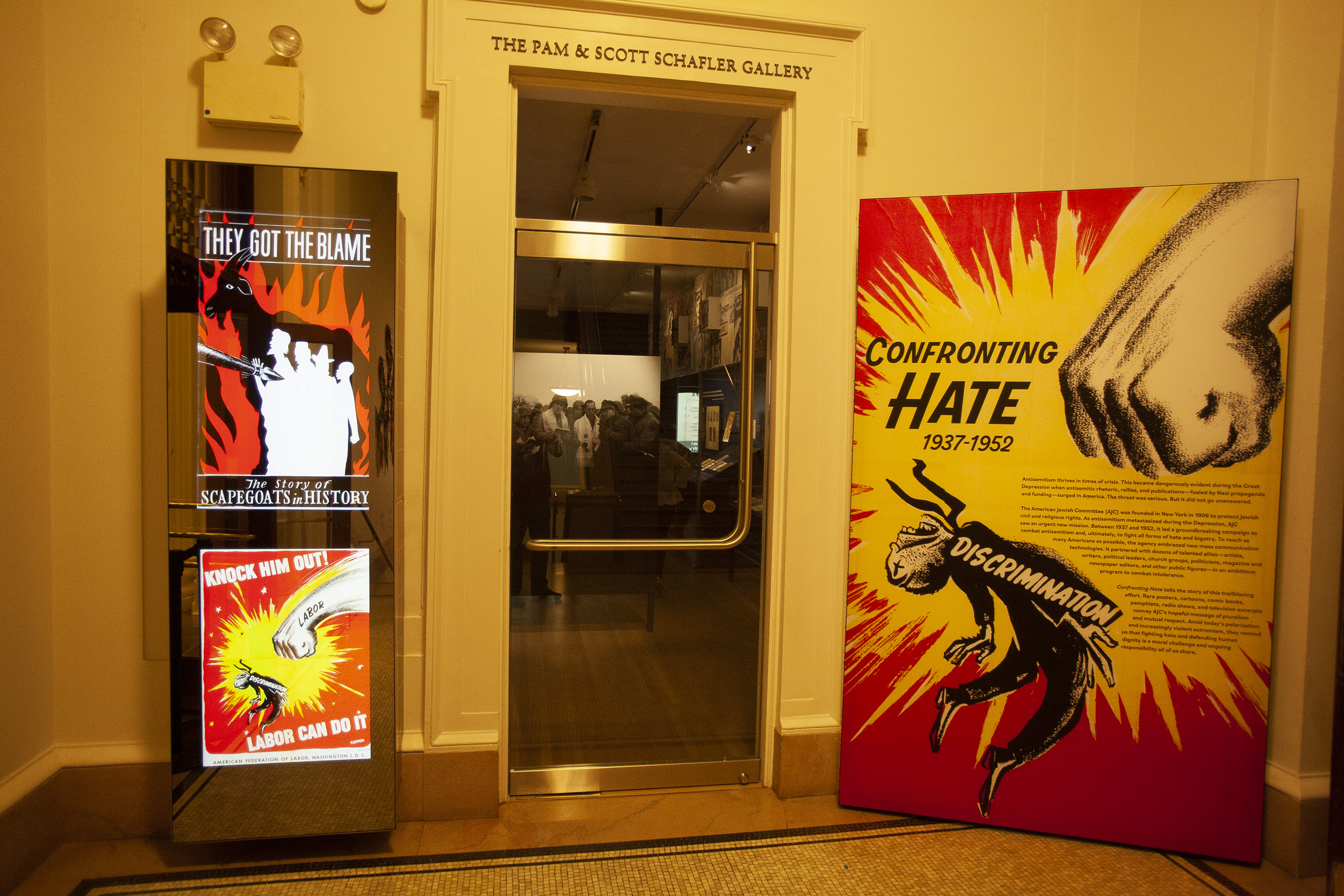 A color photo of the outside of the exhibit with a large read and white poster showing a fist marked 'labor' hitting a small person labelled 'discrimination'. 