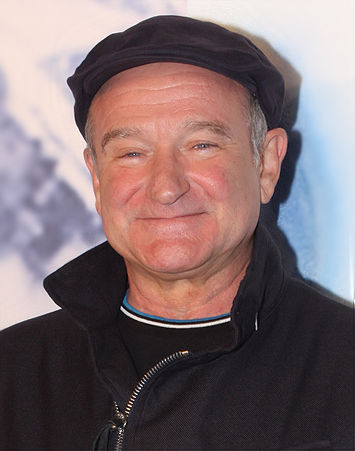 color photo of Robin Williams in portrait. He is wearing a black hat, black jacket and smiling. 