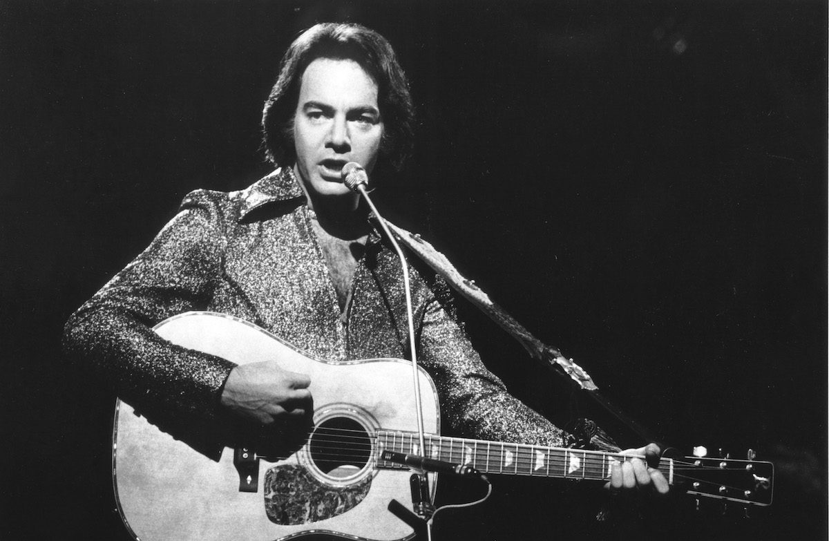 black and white photo of neil diamond holding an acoustic guitar and singing into a microphone