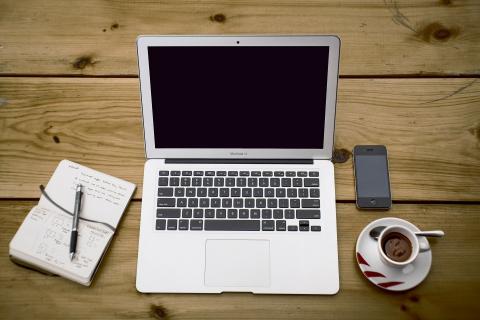 laptop on a wood table with notebook and cup of coffee next to it 