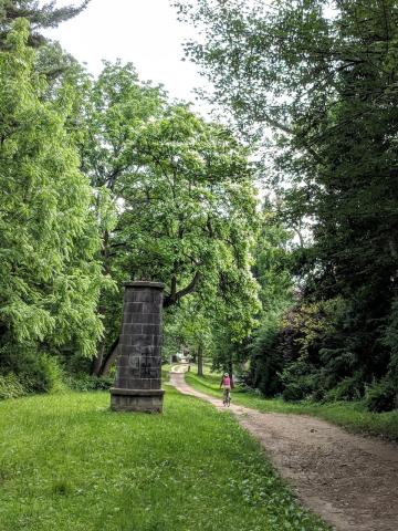 Color photo of a dirt trail thorugh a green wooded area with a stone ruin in the shape of a tower 