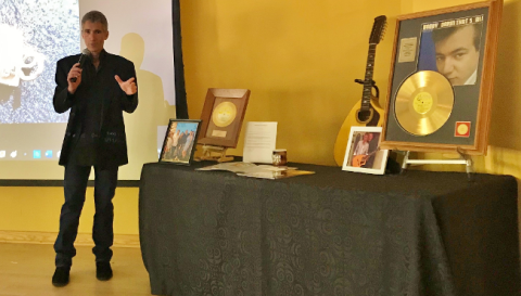 Color photo of Jimmy Scalia standing next to a table of Bobby Darin memorabilia during a presentation 