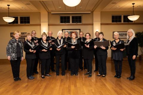 group of singers all in the black arranged on a wood floor under bright lights