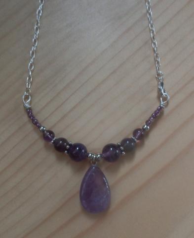 color photo of a necklace with purple beads, at the center is a larger oval shaped bead