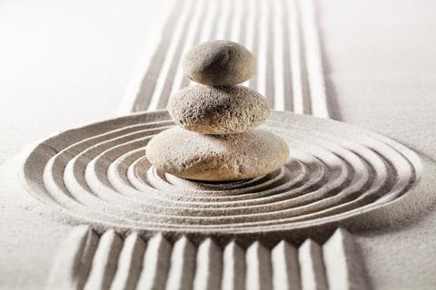 a color photograph of three stones piled by size in the center of raked sand 