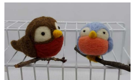 two birds made out of felt, one brown and white, the other orange and blue, perch on branches
