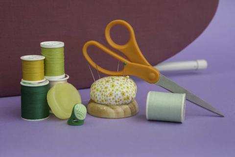 scissors, several colors of green thread and a pincushion are arranged on a purple and maroon background