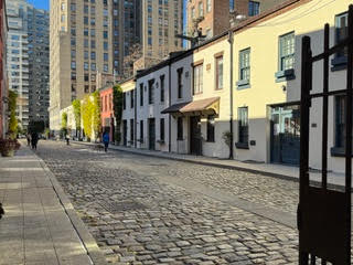 Picture of a cobblestone street with two level buildings and behind them skyscrapers