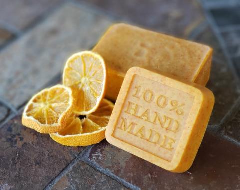 Yellow soap bars with the words '100% Homemade' pressed into them, set up next to three slices of dried lemon