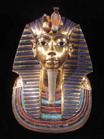 photo of king tut's gold death mask, painted in reds and blues set against a black background