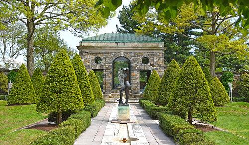 Color photo of a small stone archway with a path lined with trees 