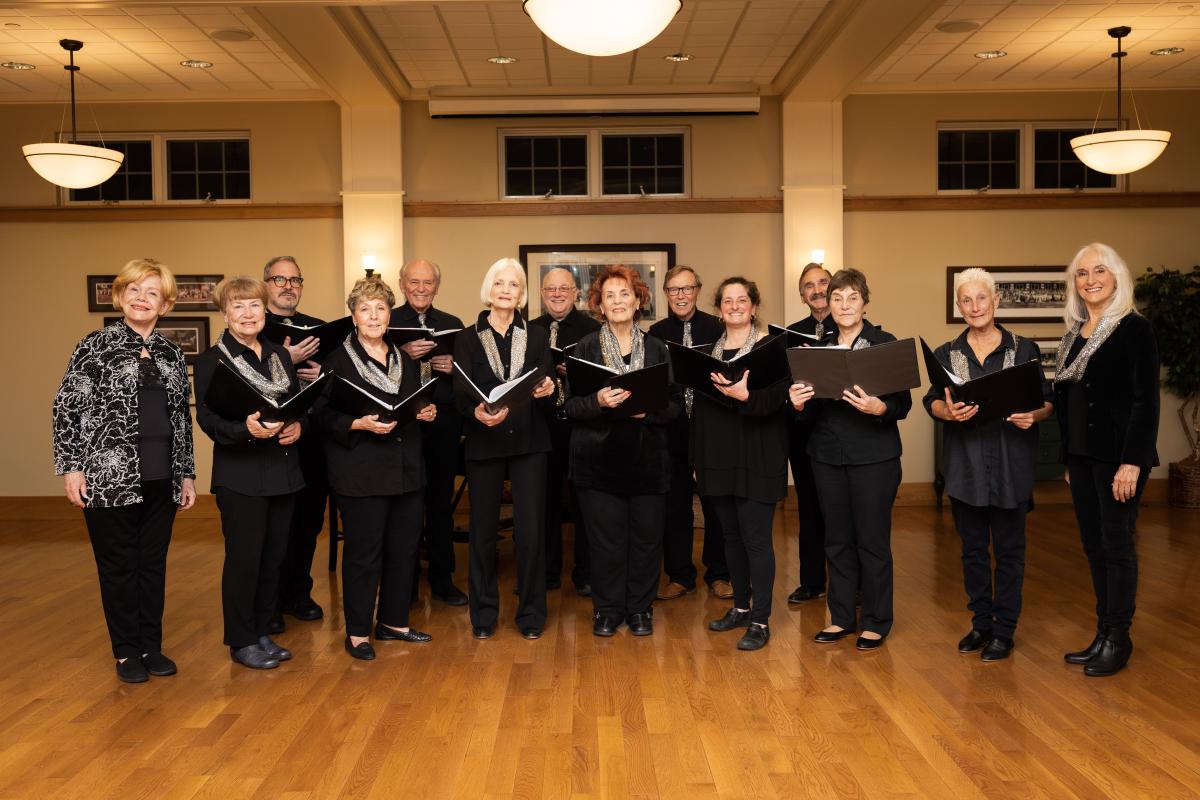 group of singers all in the black arranged on a wood floor under bright lights