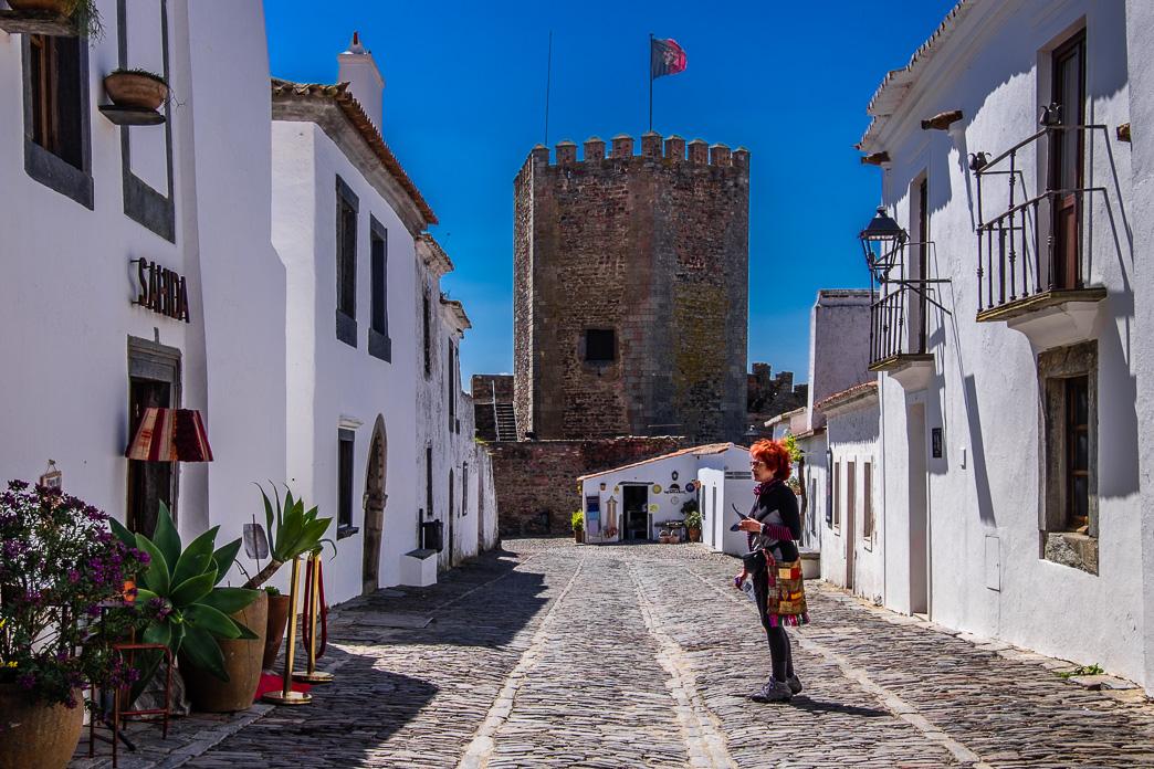 a color photo of a city street, white buildings line both sides of the road which is made of cobblestone