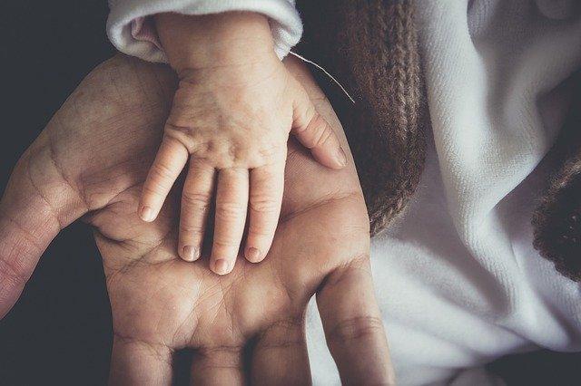 color photo of a baby's hand resting on an adult's hand