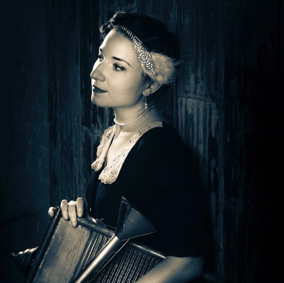 sepia profile photograph of a woman in profile wearing 1920s costume and holding a washboard